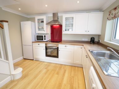 A kitchen with white cabinets wooden countertops a refrigerator microwave oven stove sink and kettle at Bryn Y Don Cottage in Benllech