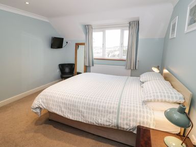 A bedroom with a double bed bedside table and lamp a chair a wall-mounted television and window with striped curtains at Bryn Y Don Cottage in Benllech