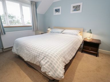 A bedroom with a double bed side tables lamps a window and framed pictures at Bryn Y Don Cottage in Benllech