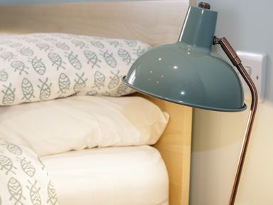 A bedside lamp next to a bed with white and patterned fish pillows at Bryn Y Don Cottage in Benllech
