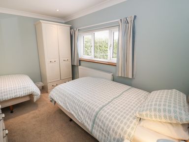 A bedroom with two single beds a white wardrobe a window with blinds and curtains at Bryn Y Don Cottage in Benllech