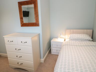 A bedroom with a single bed a bedside table with lamp a chest of drawers and a wall mirror at Bryn Y Don Cottage in Benllech