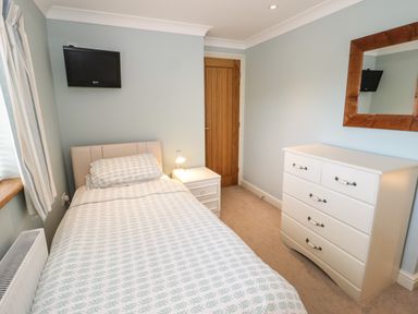 A bedroom with a single bed side table lamp dresser mirror and wall mounted television at Bryn Y Don Cottage in Benllech