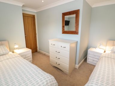 A bedroom with two single beds bedside tables lamps a chest of drawers and a wall mirror at Bryn Y Don Cottage in Benllech