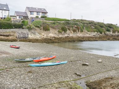 Kayaks on a rocky beach with houses and greenery on a cliff in the background at Bryn Y Don Cottage in Benllech