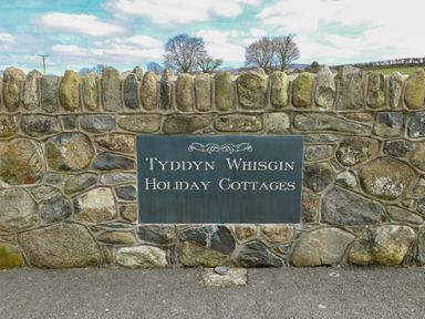 A stone wall with a sign for Tyddyn Whisgin Holiday Cottages in Caeathro near Caernarfon
