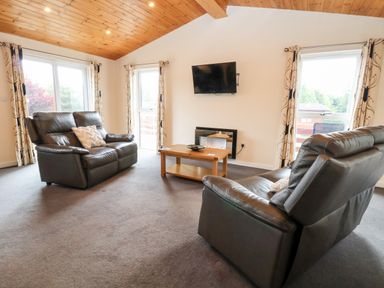 A living room with two leather sofas a wooden coffee table a wall-mounted television and large windows at Callow Lodge 5 in Beaconsfield Holiday Park