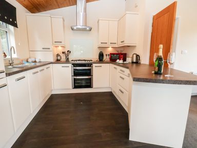 A kitchen with white cabinets dark countertops a stove a red microwave kettle and a bottle with glasses on the counter at Callow Lodge 5 Beaconsfield Holiday Park