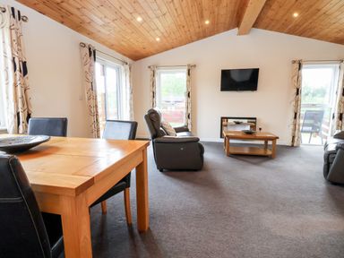 A living room with a wooden dining table and black chairs leather sofas coffee table and wall mounted TV at Callow Lodge 5 in Beaconsfield Holiday Park