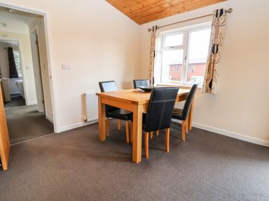 A dining room with a wooden table and four chairs near a window at Callow Lodge 5 Beaconsfield Holiday Park