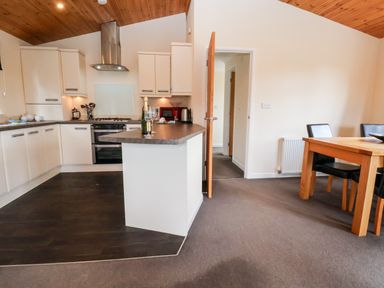 A kitchen and dining area with white cabinets a wooden dining table and black chairs at Callow Lodge 5 Beaconsfield Holiday Park