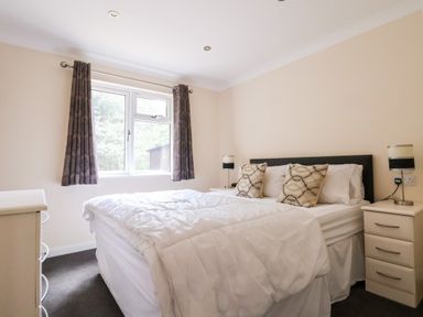 A bedroom with a double bed two bedside tables lamps and a window with curtains at Callow Lodge 5 in Beaconsfield Holiday Park