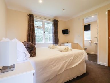 A bedroom with a bed and folded towels a window with curtains and a small television on the wall at Callow Lodge 5 in Beaconsfield Holiday Park