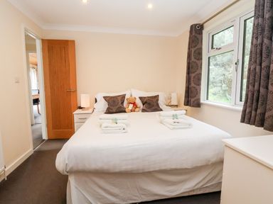 A bedroom with a double bed bedside tables lamps a window with curtains and a wooden door at Callow Lodge 5 in Beaconsfield Holiday Park