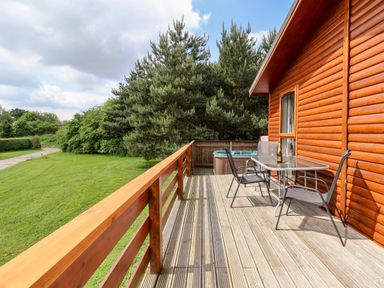 A wooden deck with two chairs a table and a hot tub beside a log cabin at Callow Lodge 5 in Beaconsfield Holiday Park
