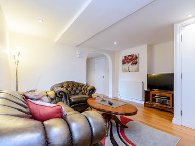 A living room with leather sofas a wooden coffee table a TV on a wooden stand and a floor lamp at Mermaid Cottage in Whitby