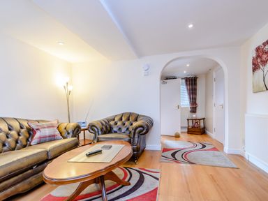 A living room with leather sofas a wooden coffee table a floor lamp and patterned rugs at Mermaid Cottage in Whitby