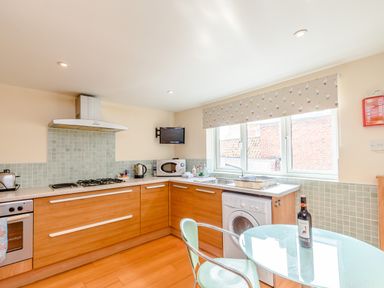 A kitchen with wooden cabinets a gas stove microwave washing machine and a glass table with two chairs at Mermaid Cottage in Whitby