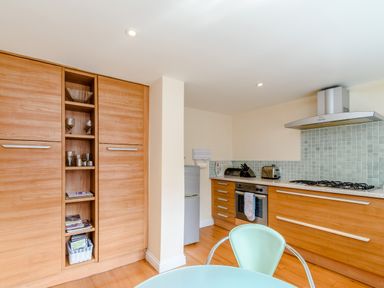 A kitchen with wooden cabinets a silver refrigerator a stove a toaster and a green chair at Mermaid Cottage in Whitby
