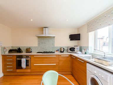 A kitchen with wooden cabinets a stove oven microwave washing machine and a window at Mermaid Cottage in Whitby