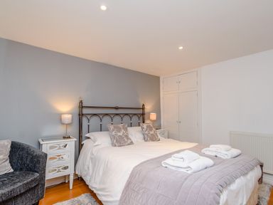 A bedroom with a double bed two bedside tables two lamps a grey armchair and a built in wardrobe at Mermaid Cottage in Whitby