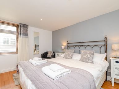A bedroom with a double bed with folded towels bedside tables with lamps a chair and a window with blinds and curtains at Mermaid Cottage in Whitby