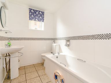 A bathroom with a bathtub a toilet and a sink with a small window covered by a blue curtain with white boats at Mermaid Cottage in Whitby