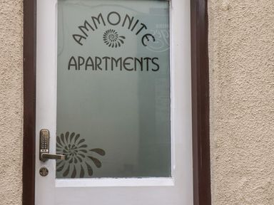A white door with frosted glass and a keypad lock with ammonite apartments text on the glass