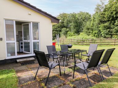 A patio with a glass table and six chairs outside a house with an open door to a kitchen at Peacehaven in Rosecraddoc Lodge near Liskeard