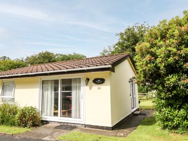 A single-story house with a tiled roof and large sliding glass doors surrounded by greenery at Peacehaven Rosecraddoc Lodge near Liskeard