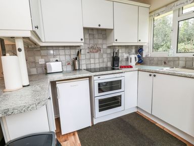 A kitchen with white cabinets a countertop with a toaster kettle knife block and paper towels at Peacehaven Rosecraddoc Lodge near Liskeard