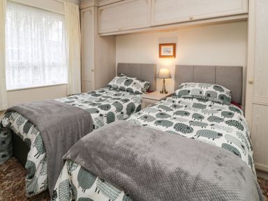 A bedroom with two single beds side by side with sheep patterned bedding and a bedside lamp at Peacehaven Rosecraddoc Lodge near Liskeard