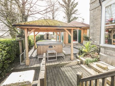 An outdoor area with a wooden gazebo covering a hot tub and benches next to a stone house at Eden Lodge in Bardsea