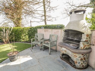 An outdoor patio with two wooden chairs a stone barbecue grill and a potted plant at Eden Lodge in Bardsea