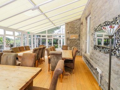 A dining room with wooden tables and chairs with a stone wall and large window at Eden Lodge in Bardsea
