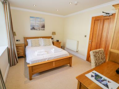 A bedroom with a wooden bed desk chair bedside tables and a closed wooden door at Eden Lodge in Bardsea