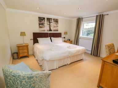 A bedroom with a double bed two bedside tables lamps a chair a desk and a window with striped curtains at Eden Lodge Bardsea