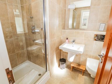 A bathroom with a shower enclosure a sink a toilet a small wooden stool and a trash bin at Eden Lodge in Bardsea