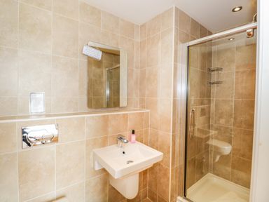 A bathroom with a wall-mounted sink, mirror, shower enclosure, and tiled walls at Eden Lodge in Bardsea