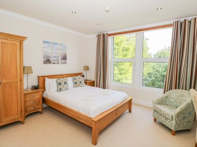 A bedroom with a wooden bed, two bedside tables, a wardrobe, an armchair, and a large window at Eden Lodge in Bardsea