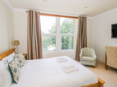 A bedroom with a wooden bed and two folded towels on it a striped curtain covering a window and two upholstered chairs at Eden Lodge in Bardsea