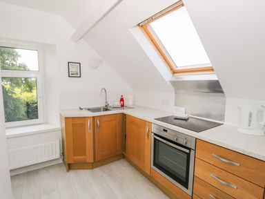 A kitchen with wooden cabinets a sink an oven a stove a kettle and windows at Eden Lodge in Bardsea