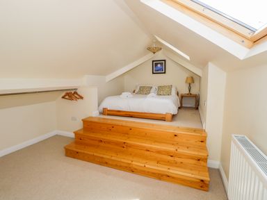 A loft bedroom with a bed on a raised wooden platform wooden hangers on a rail a bedside table with a lamp and a skylight window at Eden Lodge in Bardsea