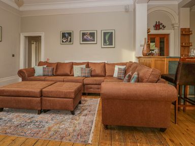 A seating area with a brown sectional sofa and ottomans on a patterned rug in a room with wooden floors at Eden Lodge in Bardsea