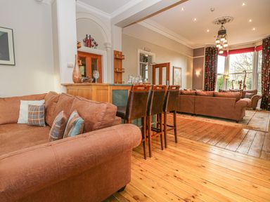 A living room with brown sofas wooden bar stools and large windows at Eden Lodge in Bardsea