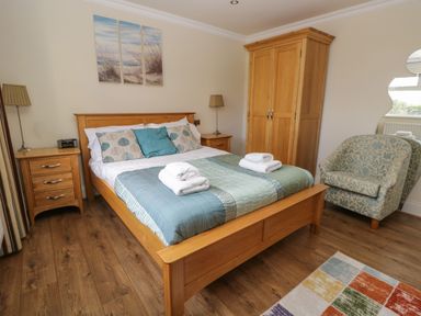 A bedroom with a wooden double bed with folded towels bedside tables a wardrobe an armchair and a patterned rug at Eden Lodge in Bardsea