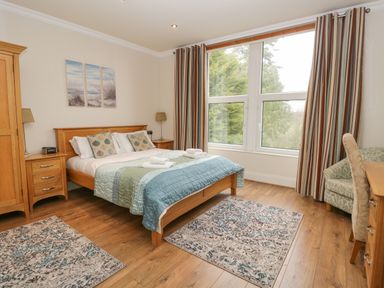 A bedroom with a wooden bed and matching furniture beside large windows at Eden Lodge in Bardsea