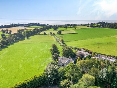 An aerial view of green fields with trees and houses near the coastline at Eden Lodge in Bardsea