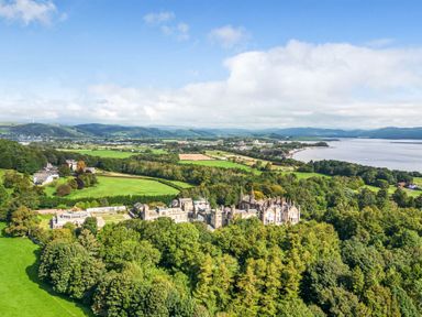 An aerial view of a large estate with a historic building surrounded by trees and fields near a body of water at Eden Lodge in Bardsea
