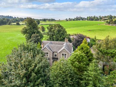A stone house surrounded by trees and green fields at Eden Lodge in Bardsea